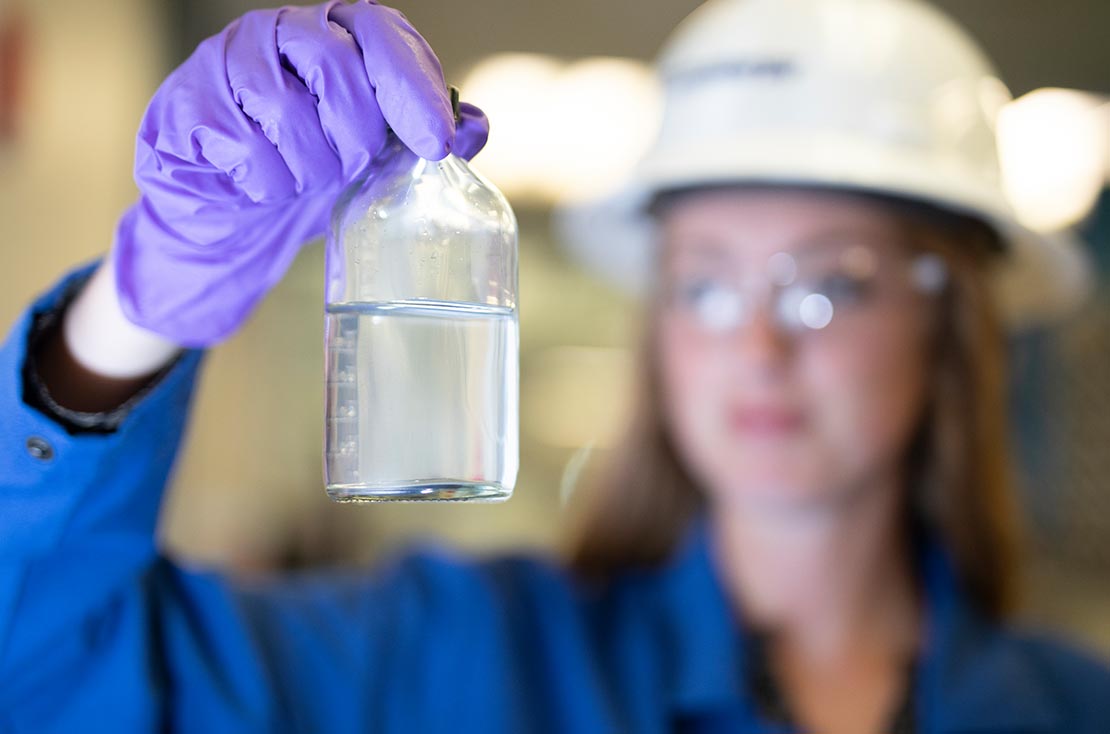 Technician holding bottle of clear water, showing impact of water clarifiers on produced water.