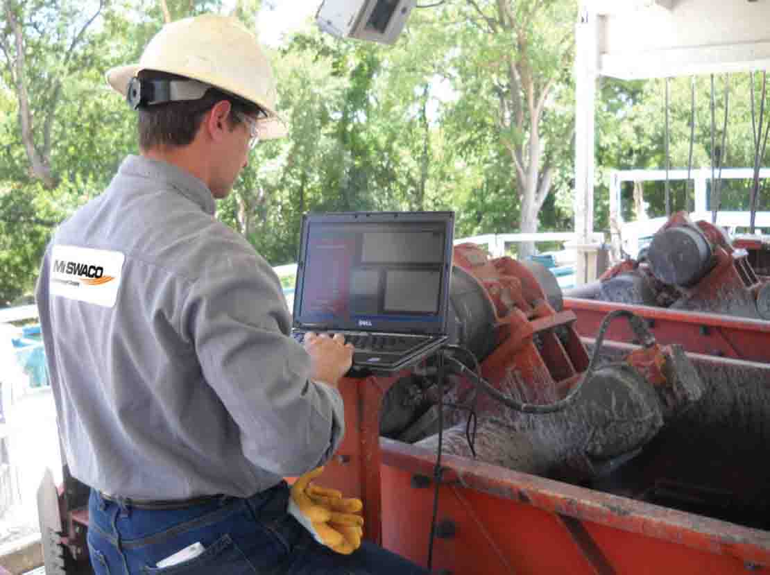 Man at computer in front of shale shaker in use.