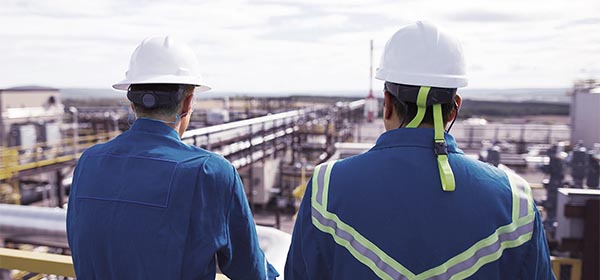 Two men in PPE looking out over onshore processing equipment.