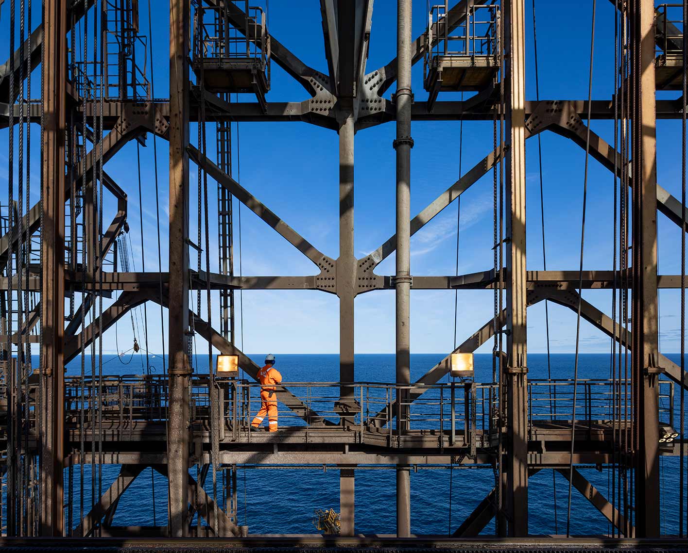 Offshore worker walking through the steel framework of an oil platform.