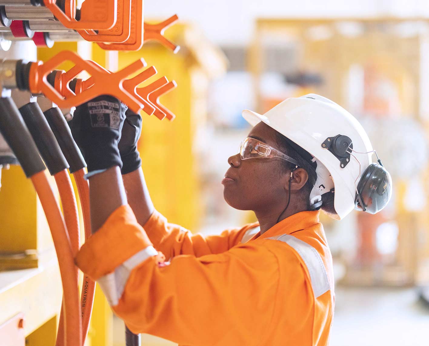 Worker in protective gear inspecting equipment at an industrial facility.