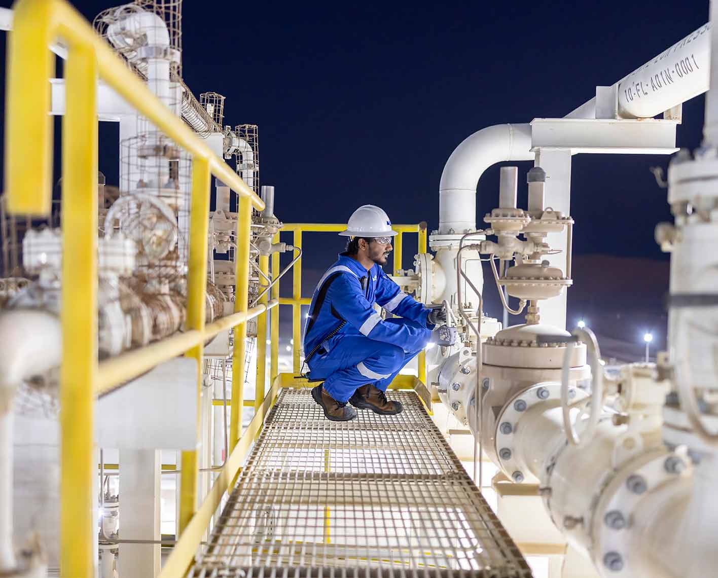 Worker inspecting industrial piping and valves at night.