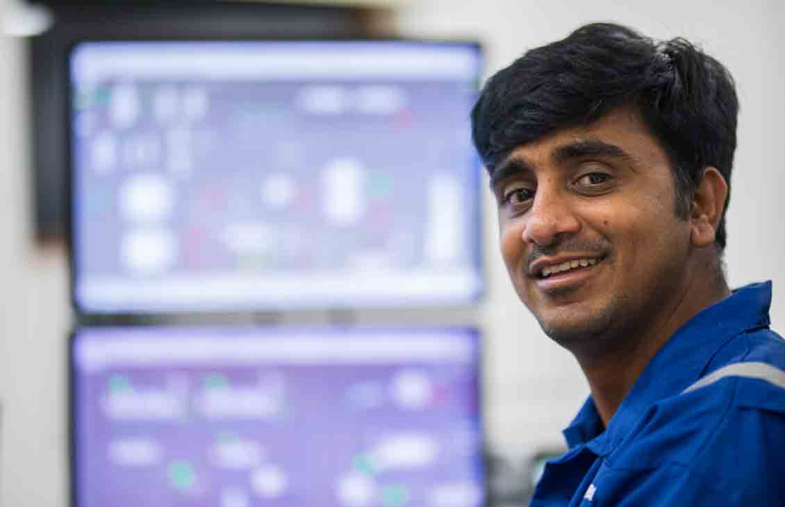 A Schlumberger engineer, with dual-display in the background showing process flow optimization software.