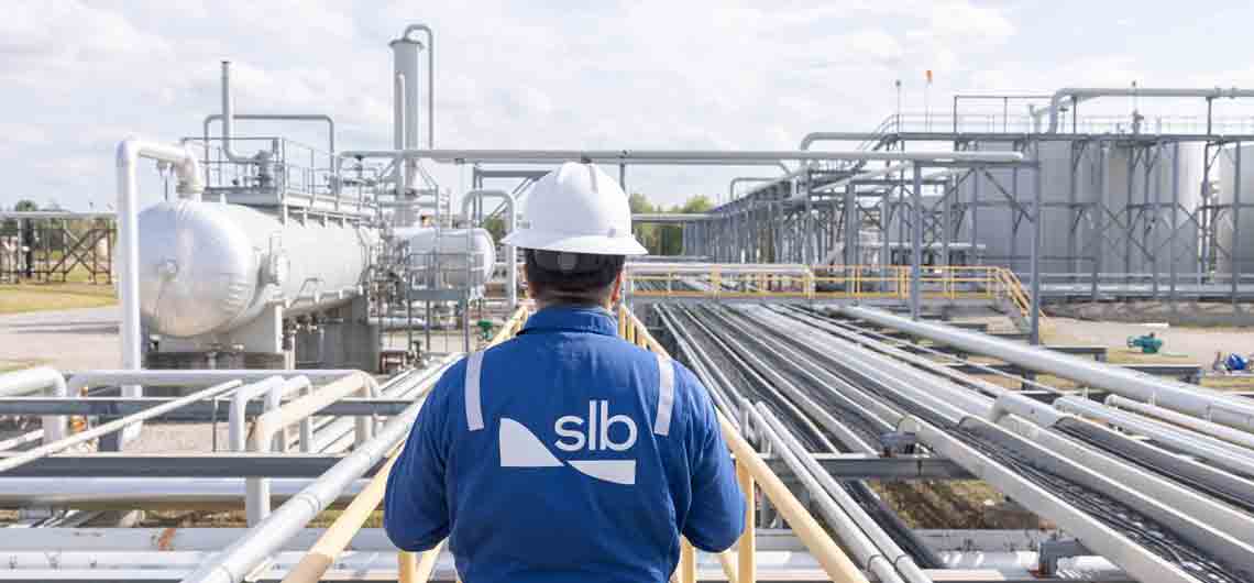 Rear view of an SLB operative looking out at pipelines and tanks in a process facility.