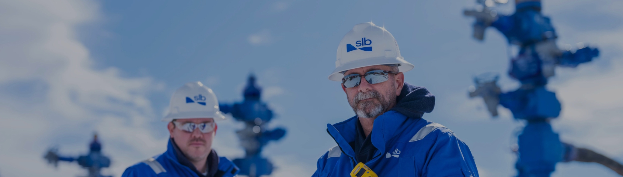 Image of 2 men in an oilfield with wellheads behind them