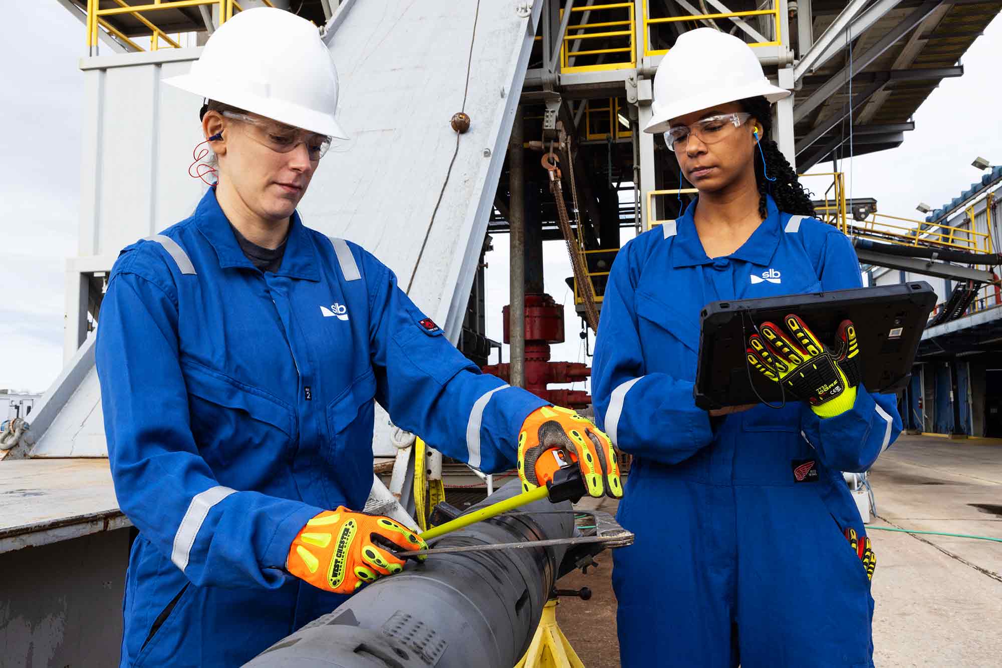 Two female SLB employees prepping a wireline tool in the field.