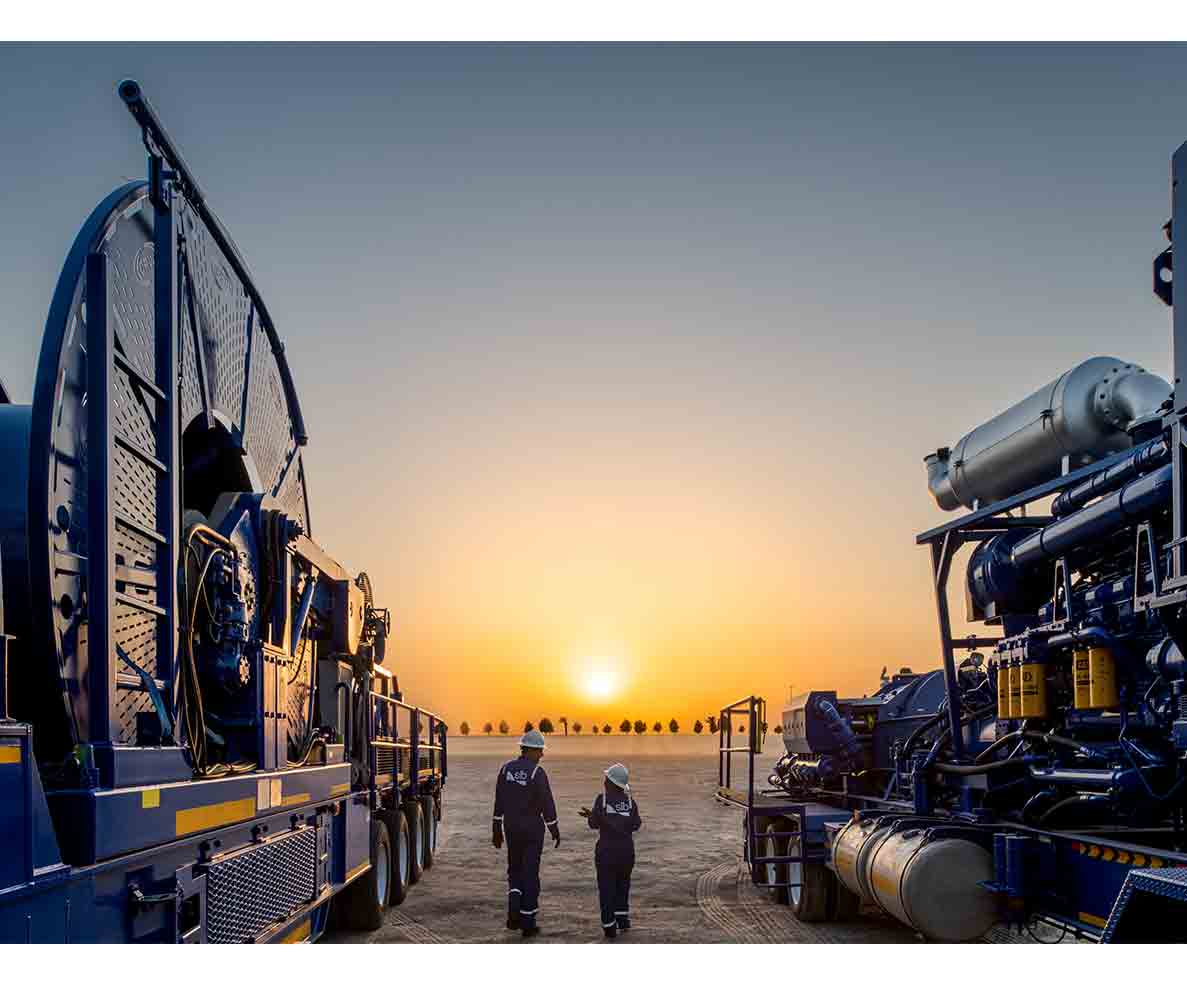 Two people walking toward the sunset next to coiled tubing equipment