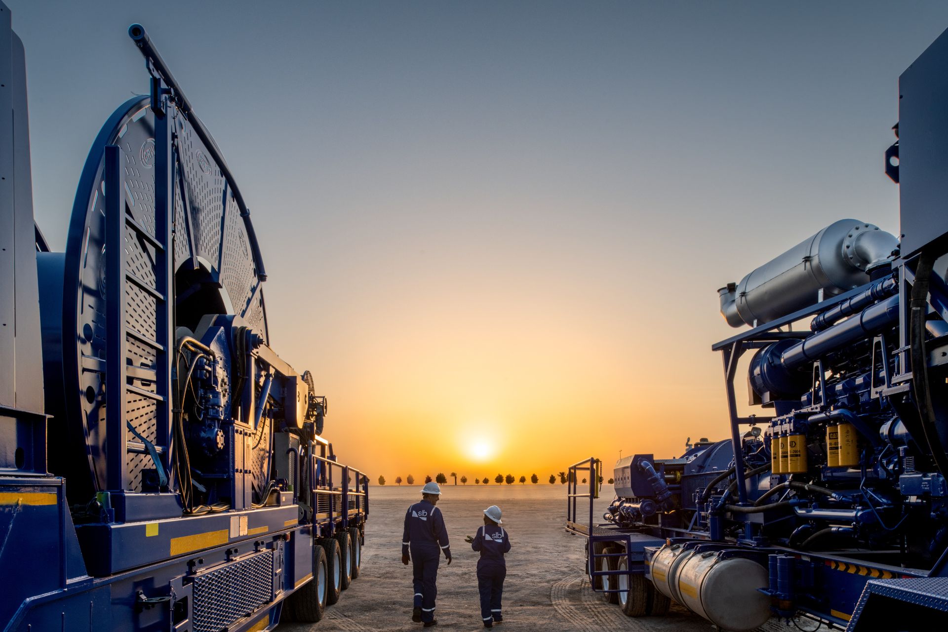 Photo of two people walking between coiled tubing units in the Middle East.