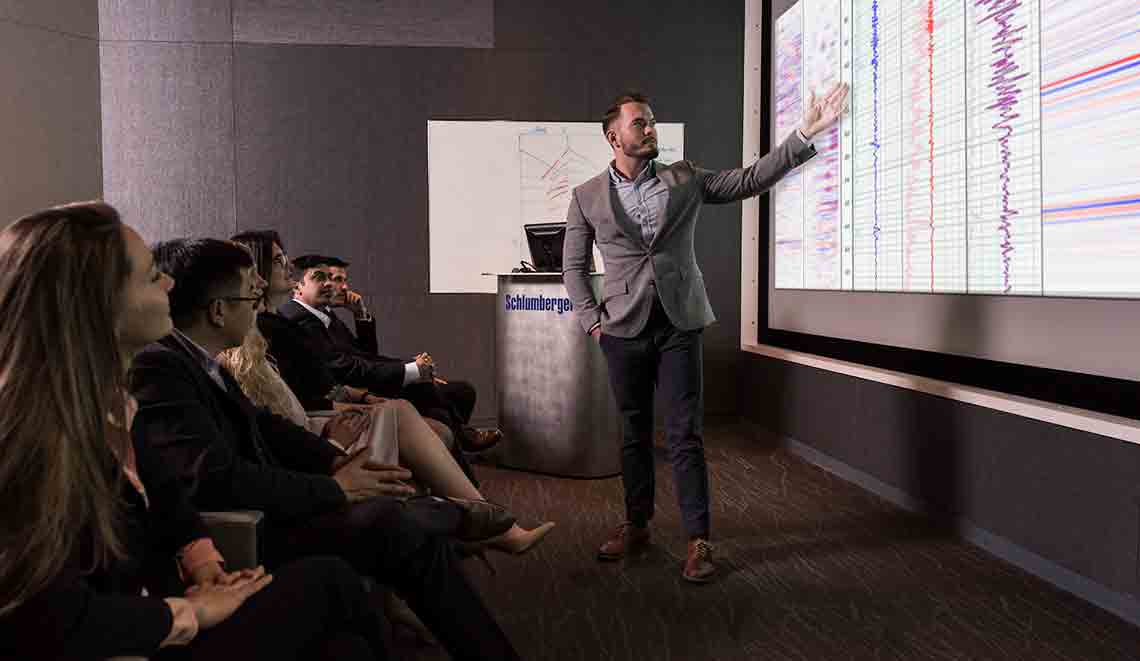 Presenter giving a speech to a crowd with seismic data in the background