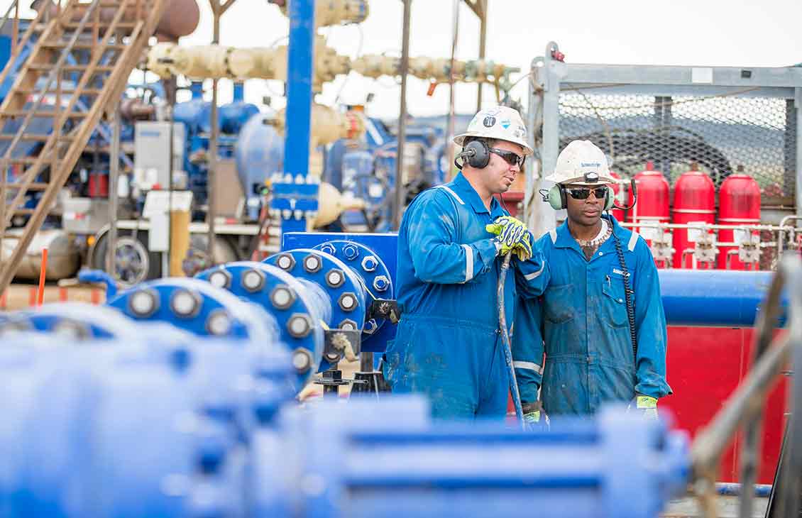 Two Schlumberger Workers on Rigsite Standing Near Equipment