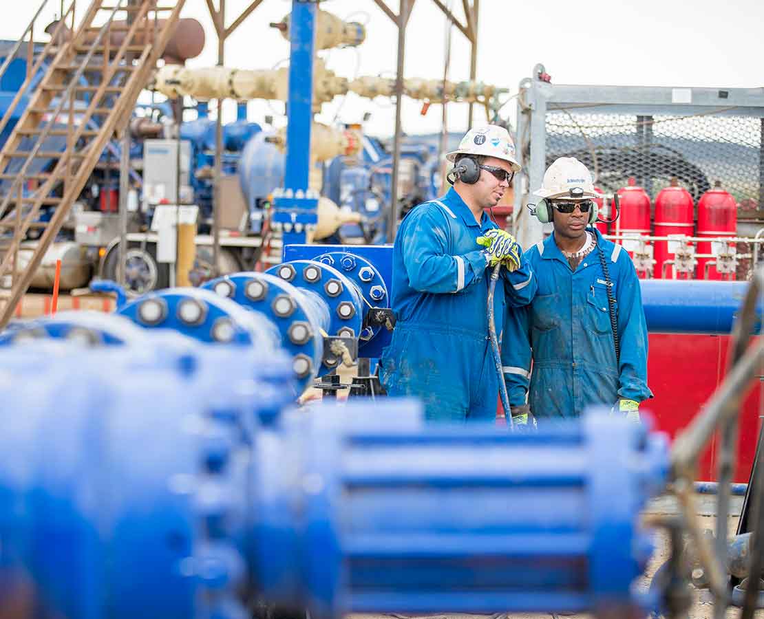 Two Schlumberger Workers on Rigsite Standing Near Equipment