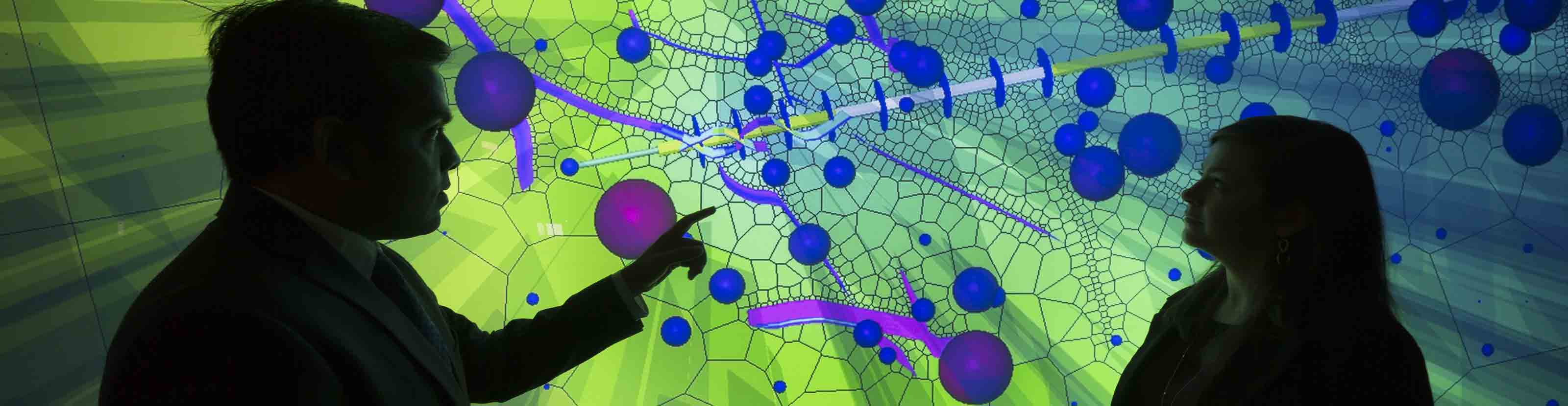 Two Schlumberger employees pointing to fractures on a 3D Petrel plot of a refracturing job.