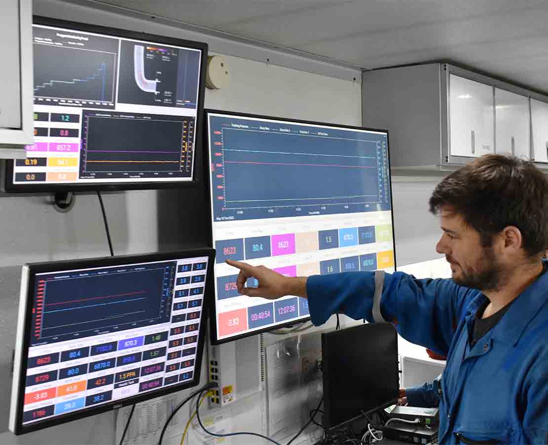 Schlumberger worker using FracCAT fracturing computer-aided treatment system while looking at monitors on rigsite.