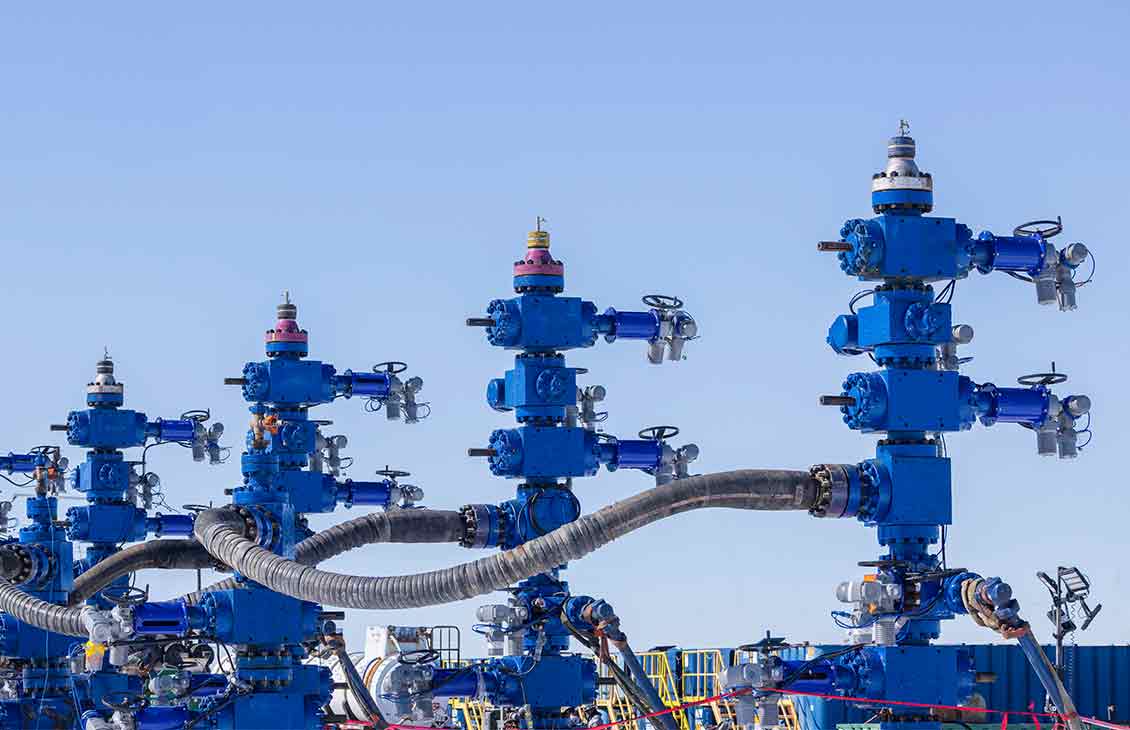 Photo showing a row of frac trees on a well pad.