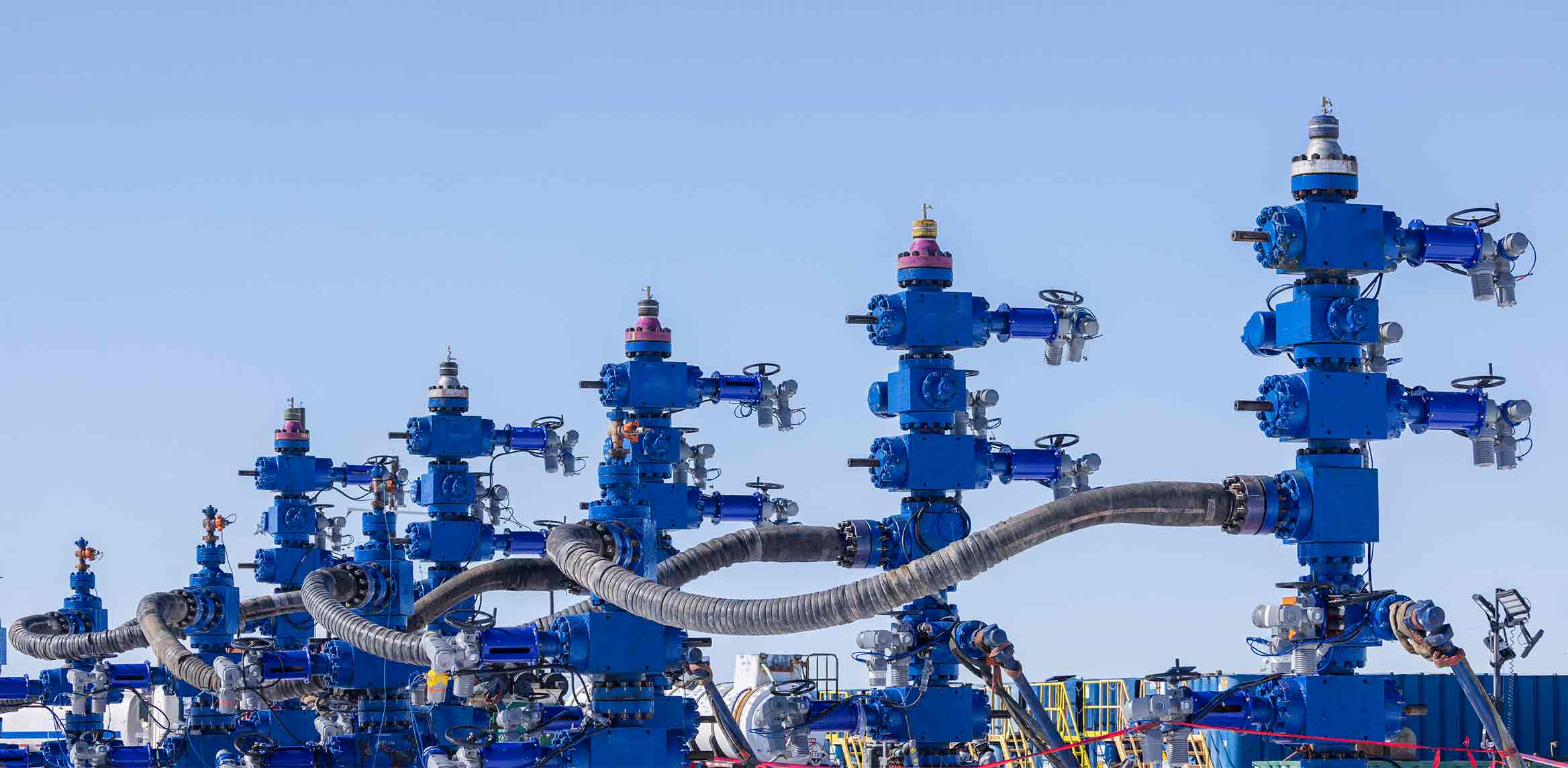 Photo showing a row of frac trees on a well pad.