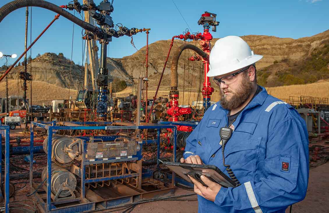 Cameron operator looking at a tablet screen in front of frac trees