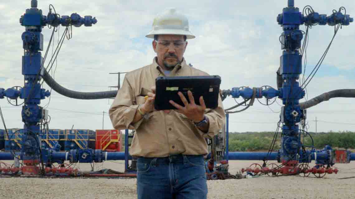 Photograph of man with tablet tracking and controlling operations using the frac trees behind him.   