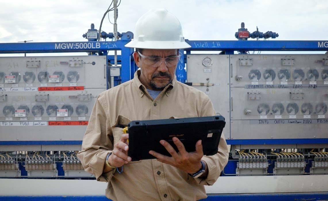Operator working on a tablet with frac trees behind him.