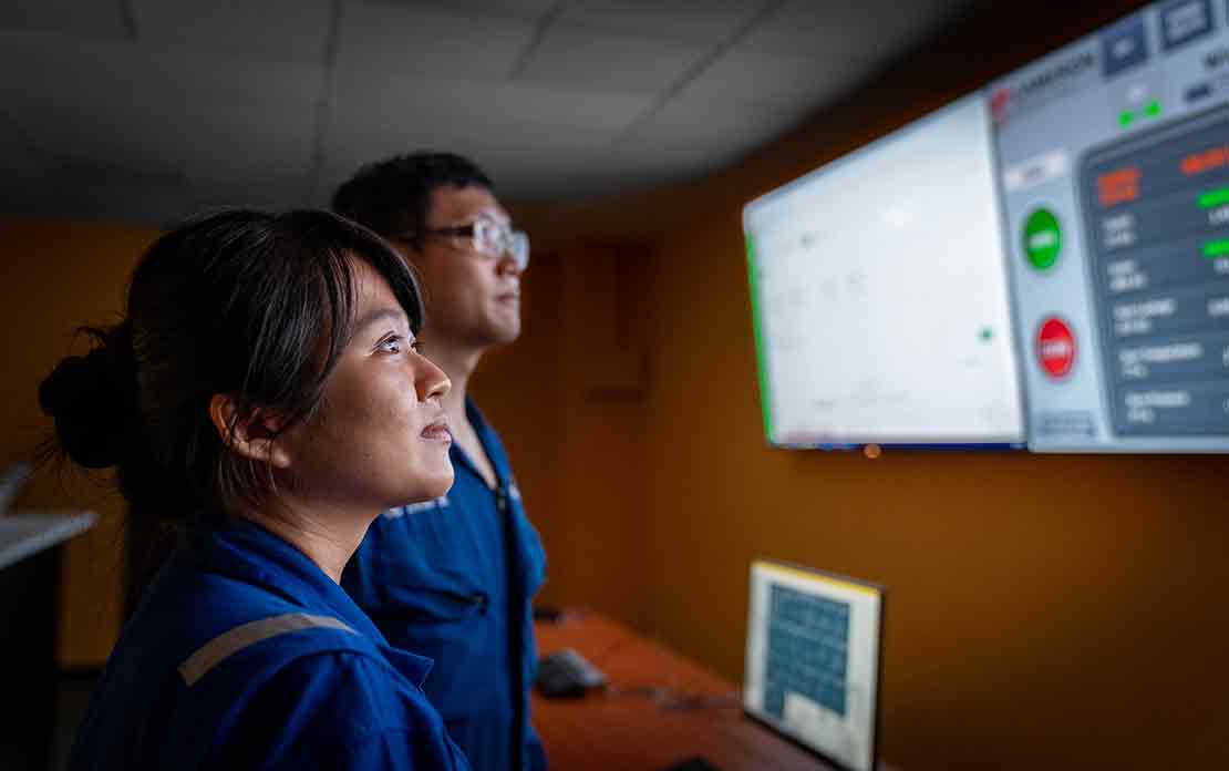 2 Schlumberger engineers—a male and a female—examining data displayed on a monitor.