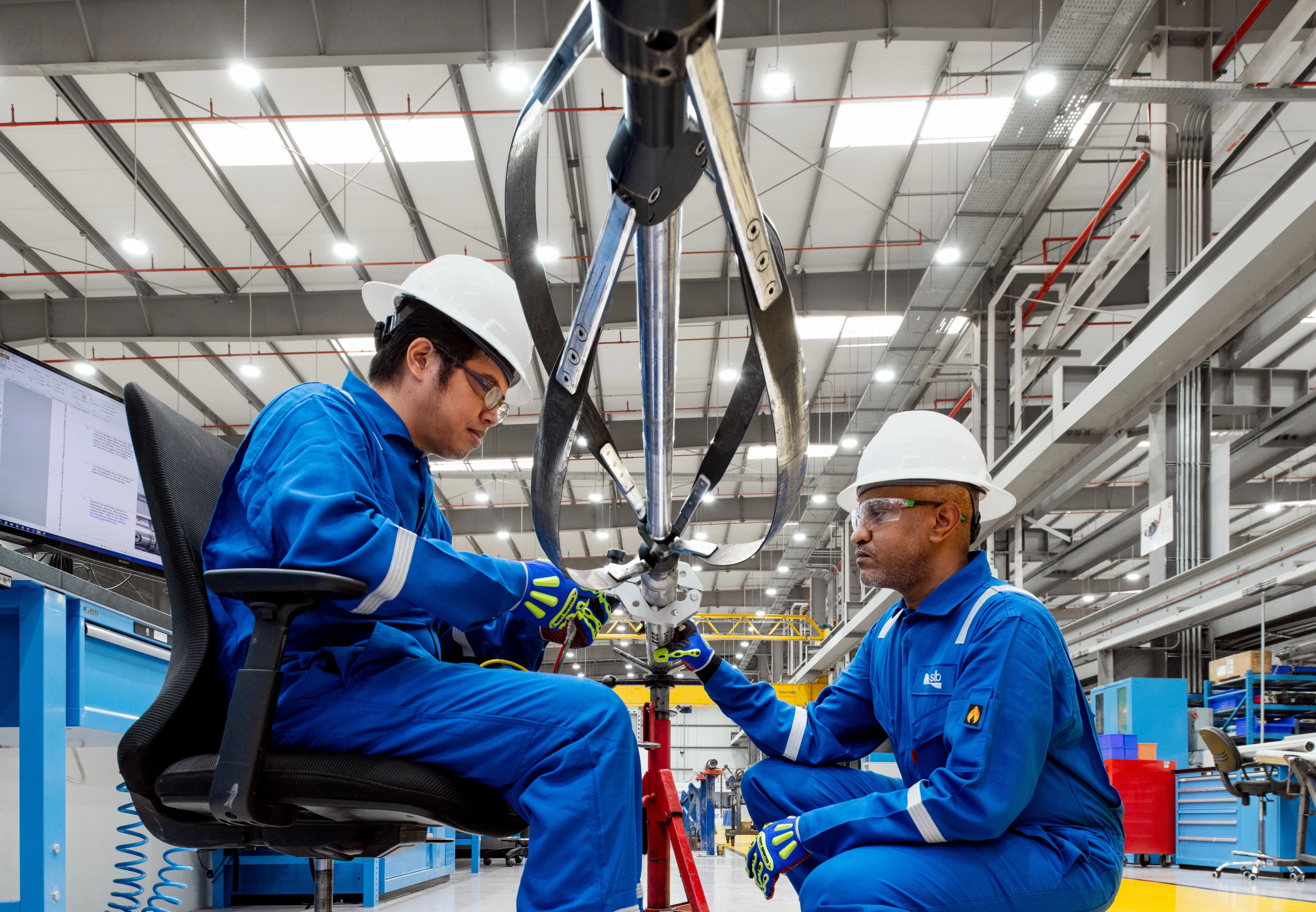 Two SLB employees in blue coveralls working to fix machinery