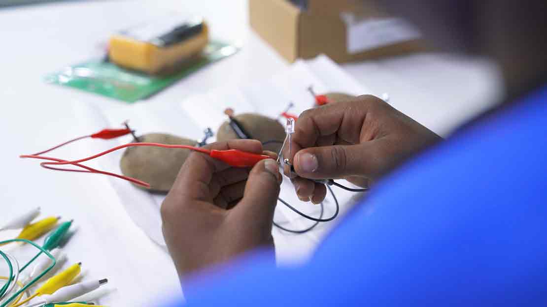 Child's hands connecting wires to an LED for an electrical experiment.