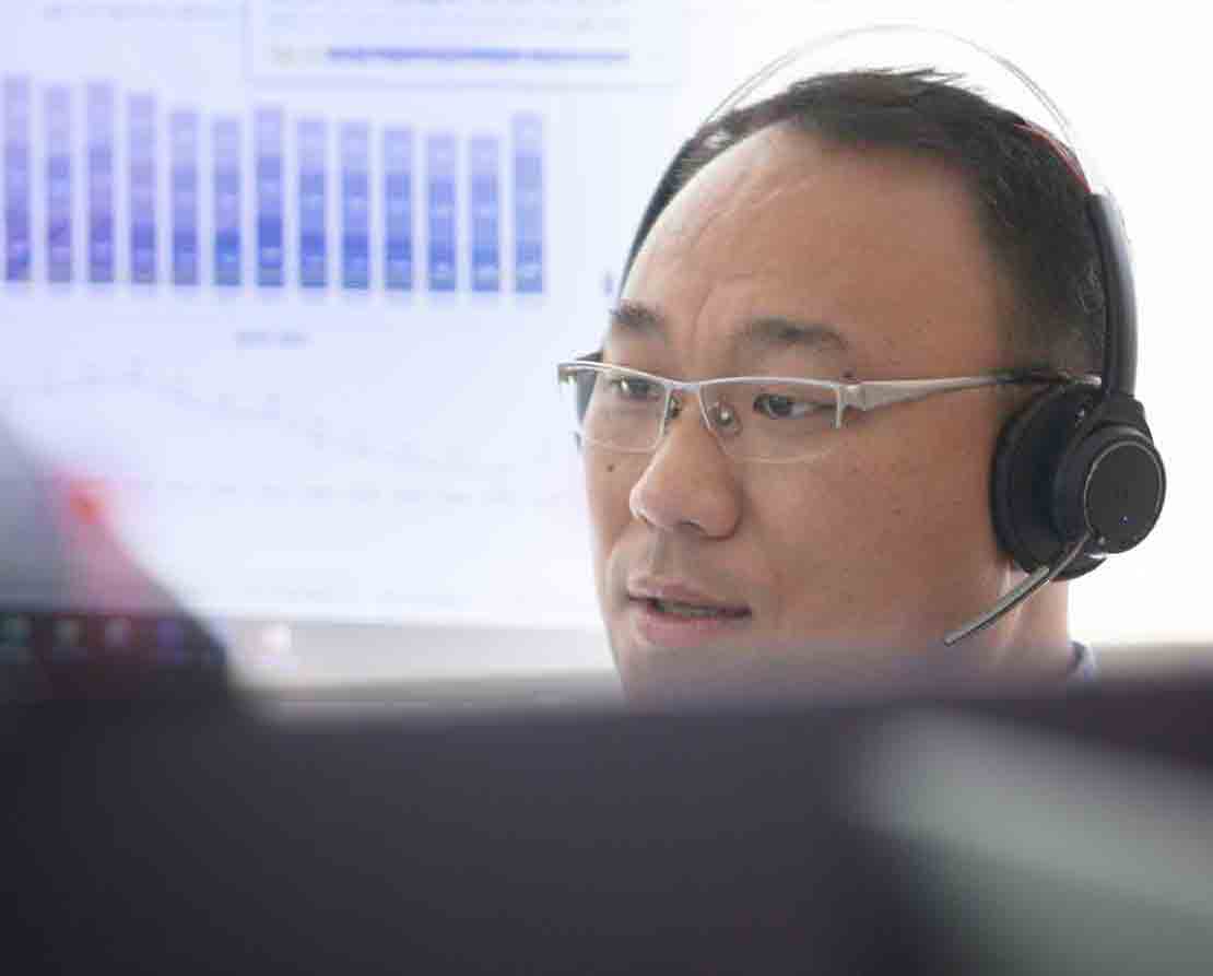 A global support tema member wearing a headset with a data screen in the background
