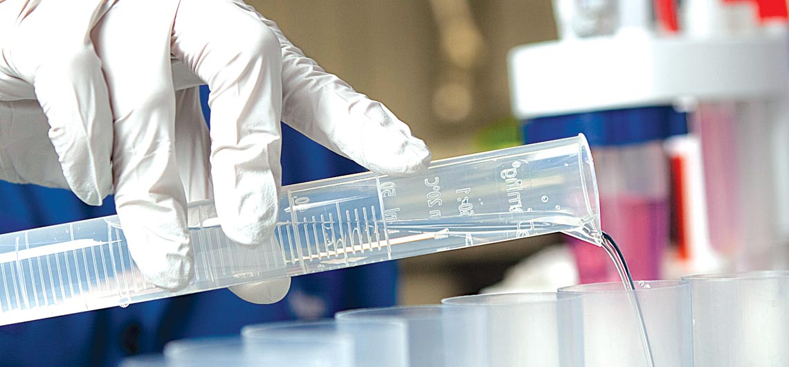 Schlumberger worker in lab pouring fluid from lab equipment while performing compositional analysis.