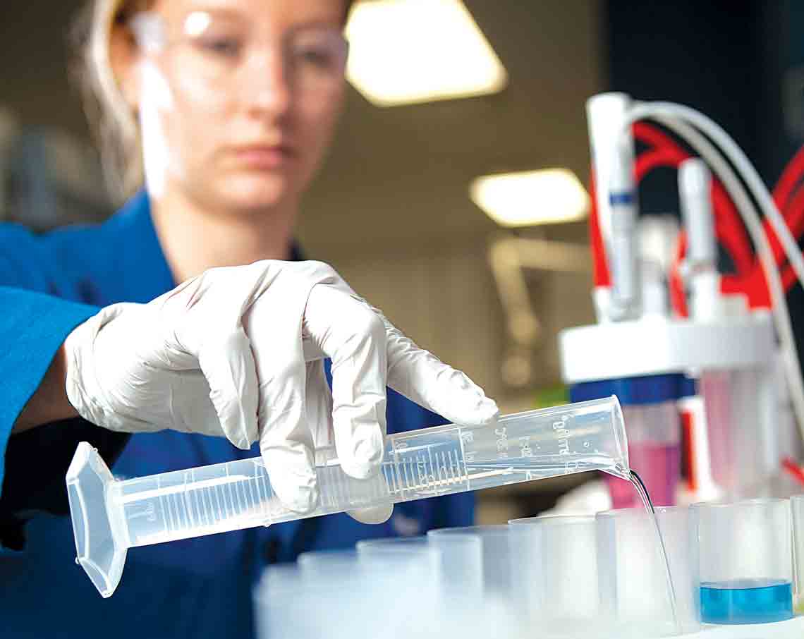 Schlumberger worker in the lab pouring a fluid as part of geochemical interpretation.