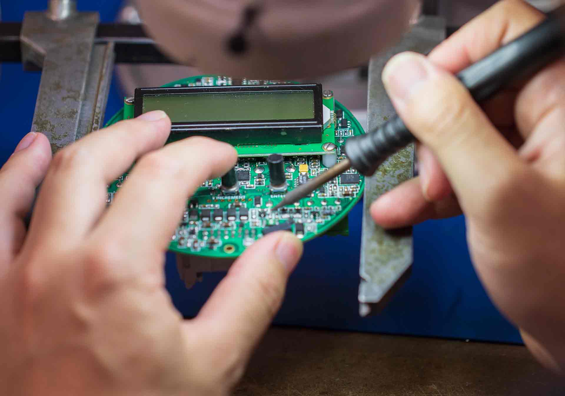 Photo shows a pair of hands soldering a circuit board in a metering device.