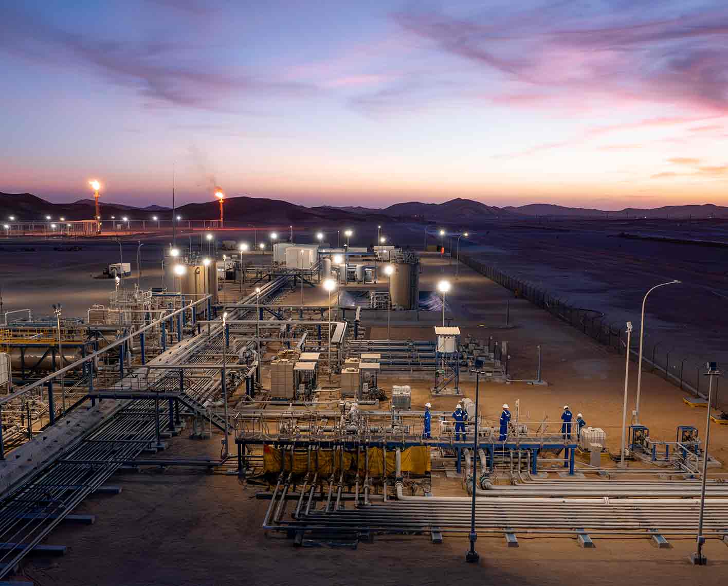 Evening view of a small processing site in the desert with several SLB personnel.