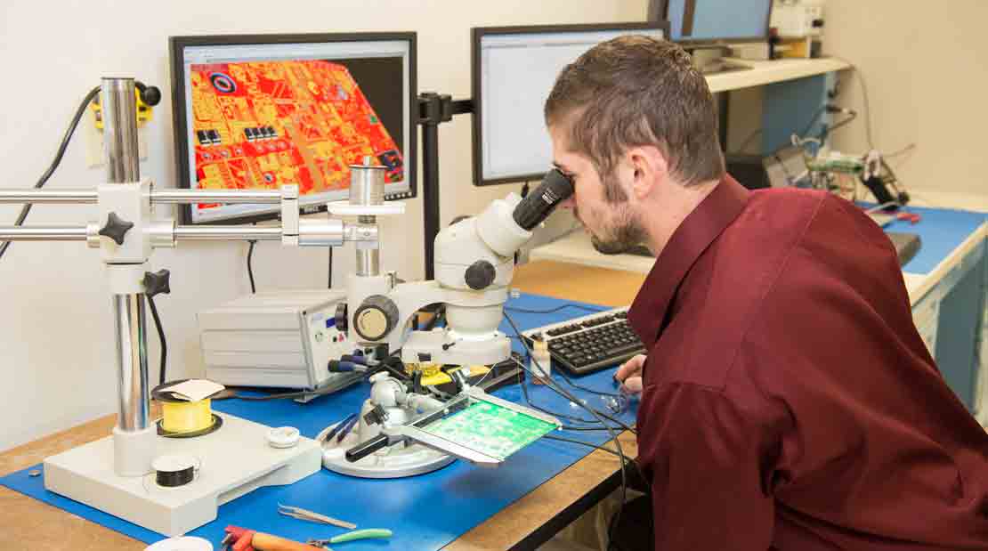 Technician looking at a circuit board through a microscope