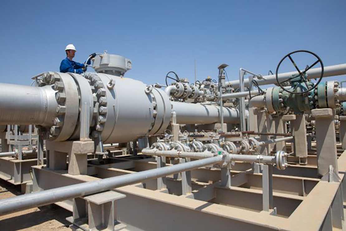 SLB employee standing near large valve equipment at a processing facility.