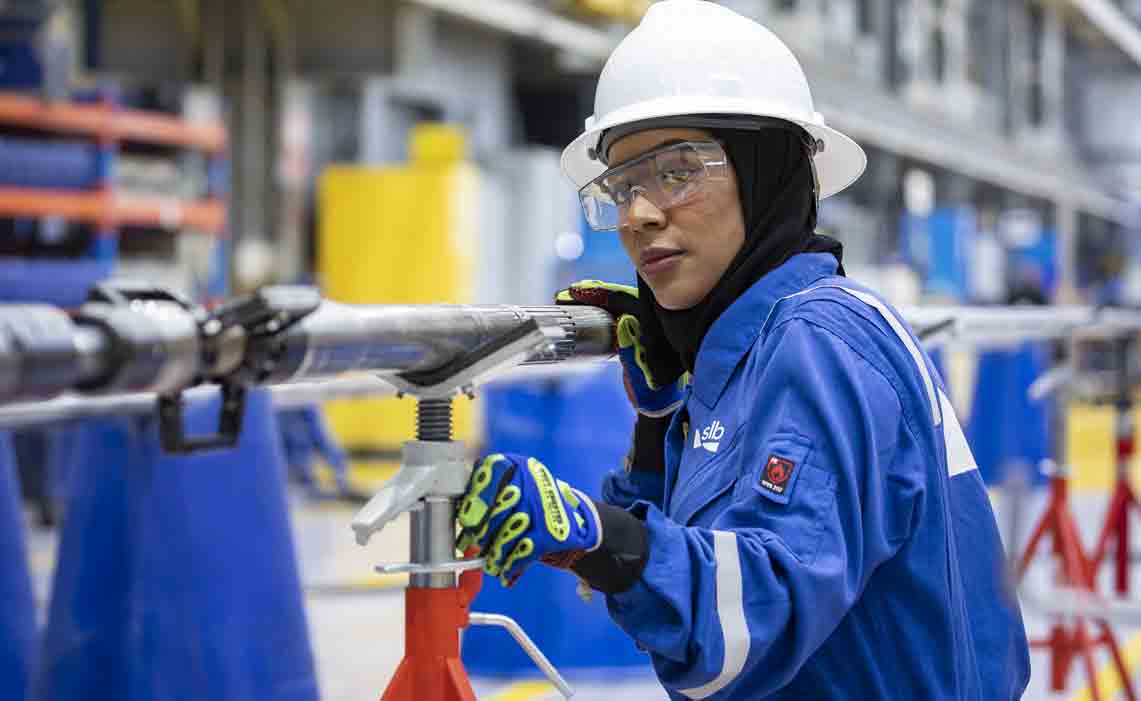 Female SLB field employee with SLB blue coveralls and a white hard hat on